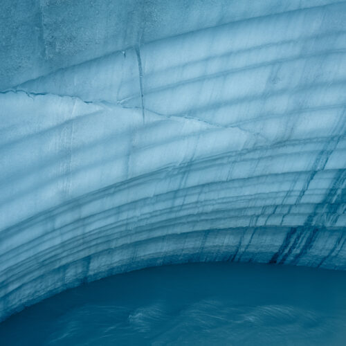 Coatings of glacier ice layering on top of each other above a glacier blue stream